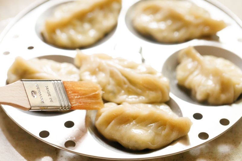Butter being brushed on steamed paneer momos.