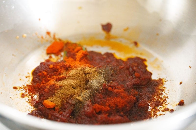 mix of ground spices on tomato paste in pan.