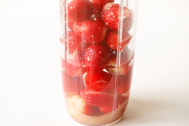 Water with strawberries and sugar in a blender cup.