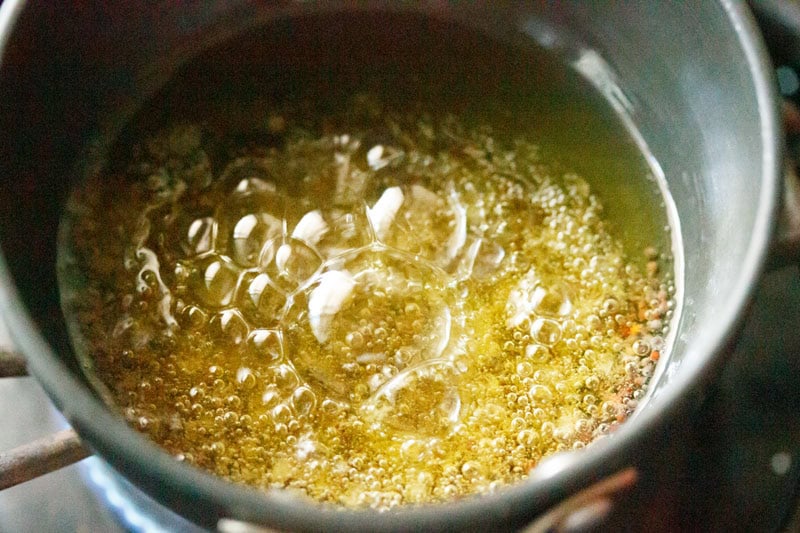Oil bubbling in a pan with mustard seeds crackling in it.