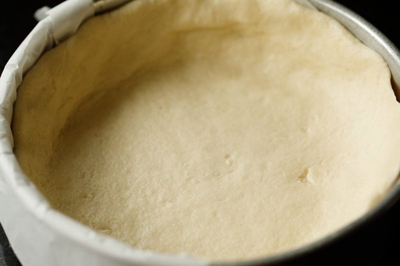 deep dish pizza dough lined on parchment on baking pan.