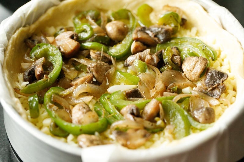 Unbaked pizza with sautéed onions, bell peppers and mushrooms.