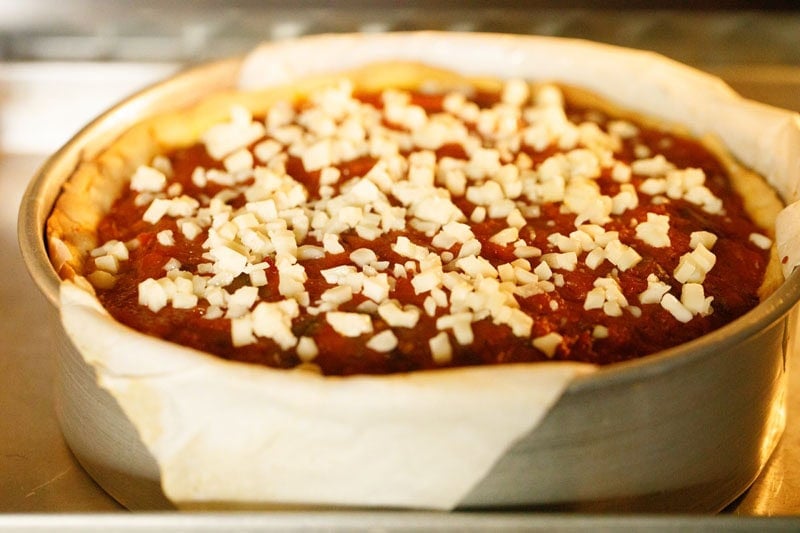 Deep dish pizza with cheese topping in oven.