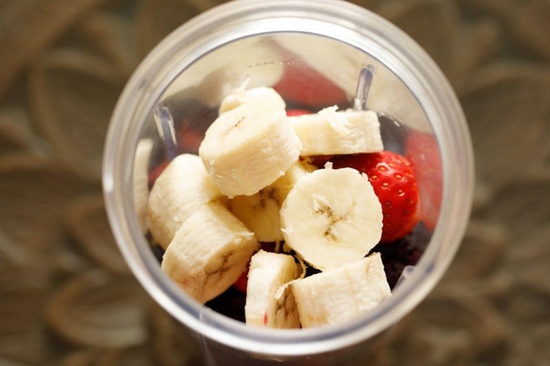 Banana and strawberries in a blender cup.