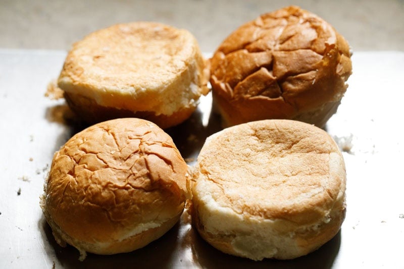 Four burger buns on chopping board.