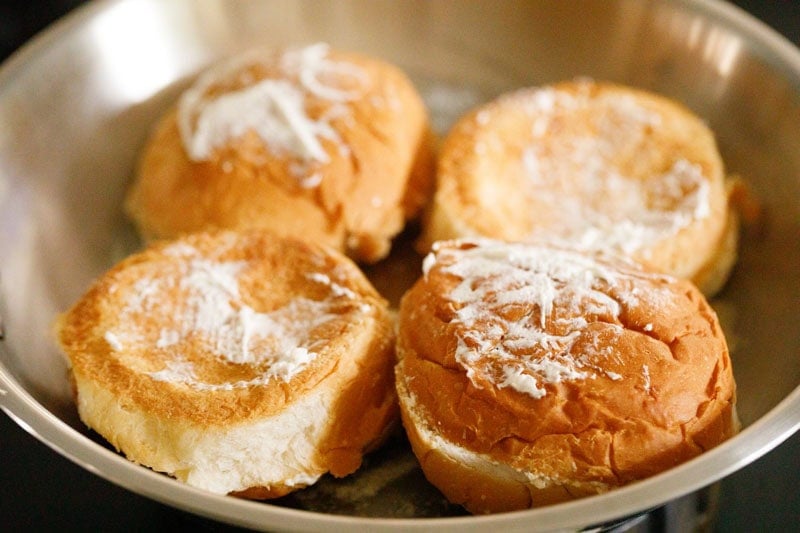 Four buttered buns in a pan with butter spread on top of each bun.