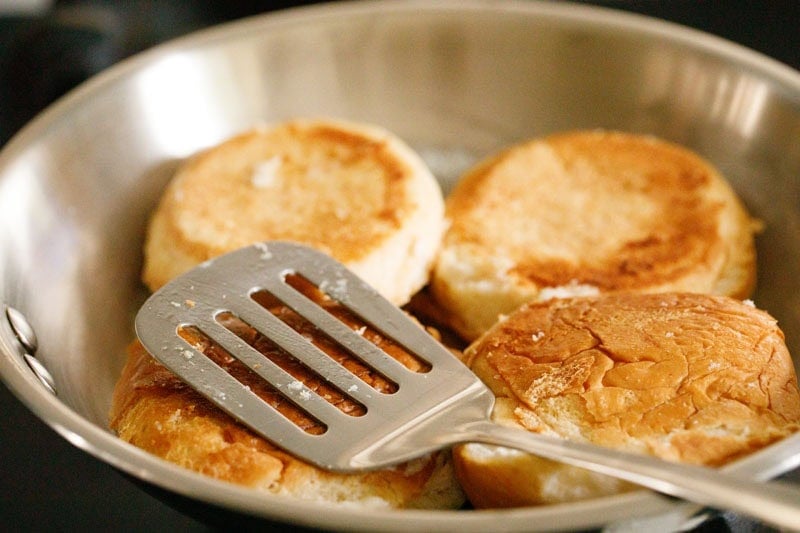 Toasted buns in a frying pan with a spatula on top.