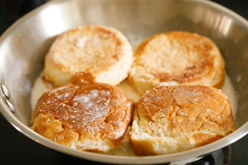 Buns in a frying pan with milk at the bottom.