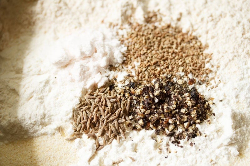 Cumin, carom seeds and crushed black pepper on top of flour.
