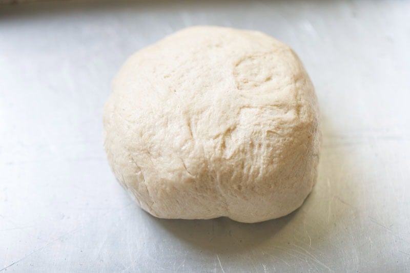 Round ball of dough on baking tray surface.