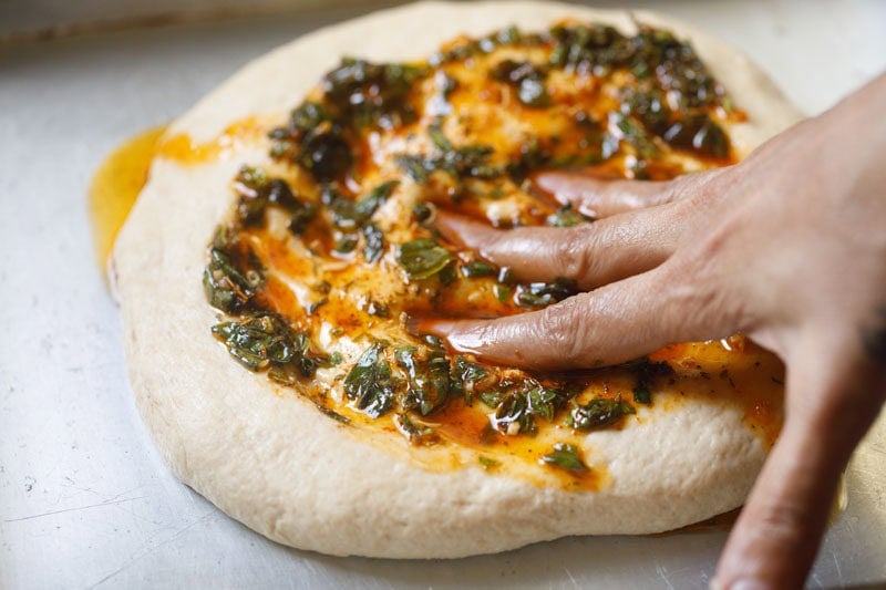 Hand pressing herb oil into dough.