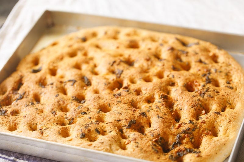 Golden-brown baked focaccia bread in tray.