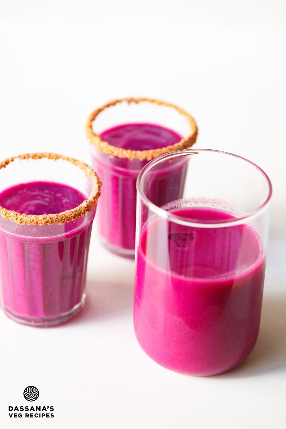 Jamun juice in a tall glass with two jamun shots glasses in the background.