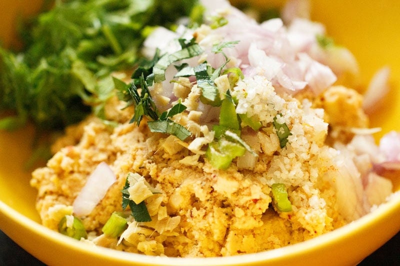 Onions, ginger, herbs and salt added to the masala vada mixture in bowl.