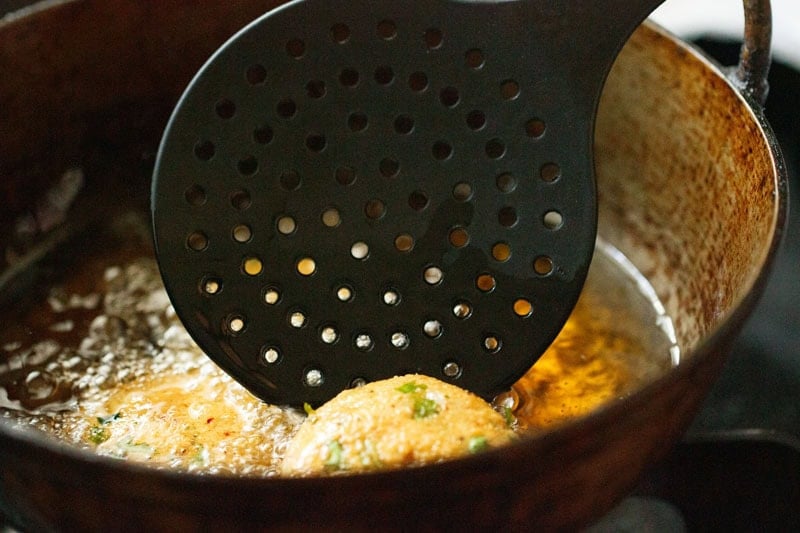 Frying masala vada with a slotted spoon turning the vada.