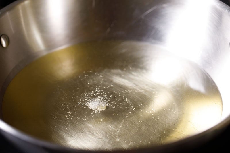A small piece of potato in hot oil in a frying pan.