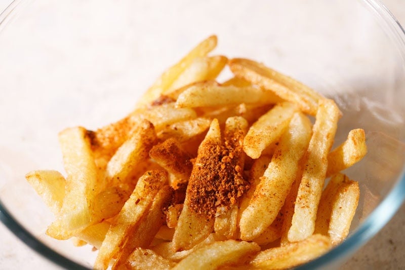 Crispy and golden fries in a bowl with peri peri seasoning on top.