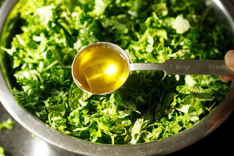 Spoon with olive oil with parsley bowl underneath.