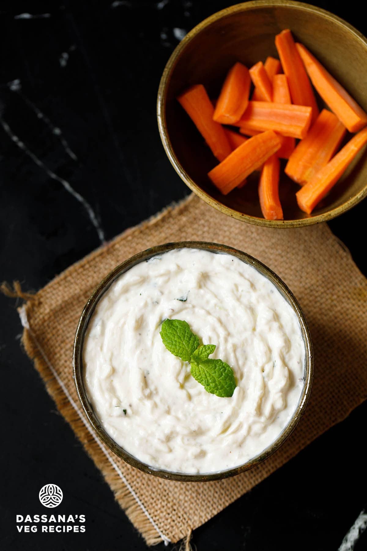 tzatziki in a bowl with garnish of mint sprig and bowl of bright orange carrot sticks.