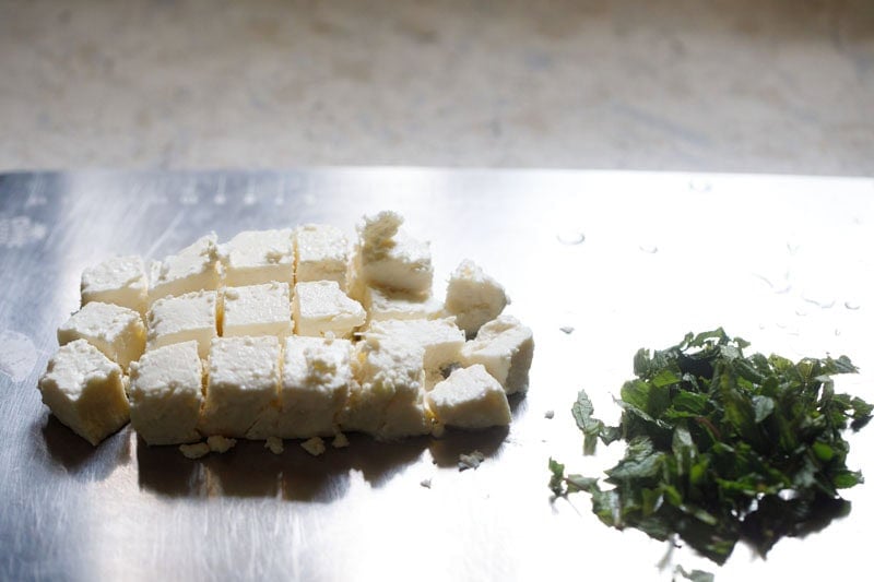 Feta cheese block chopped into chunks and mint leaves chopped on a metal tray.
