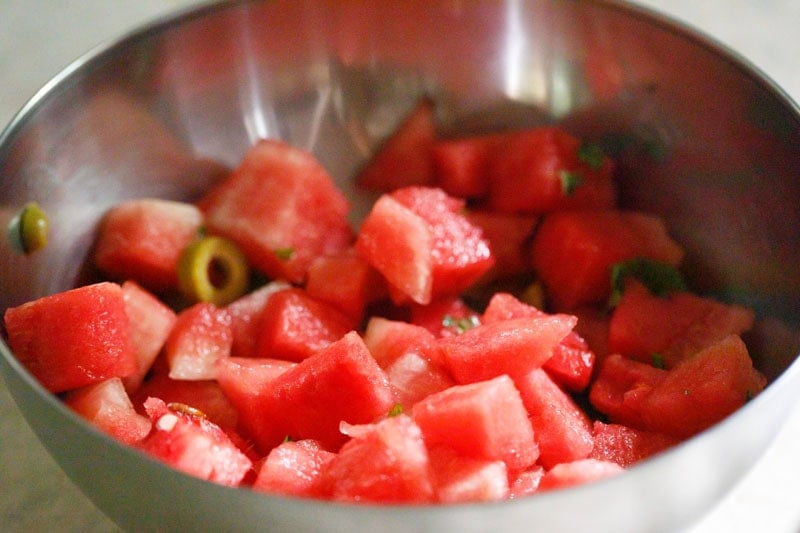 Bowl of diced watermelon pieces mixed with olives and mint.