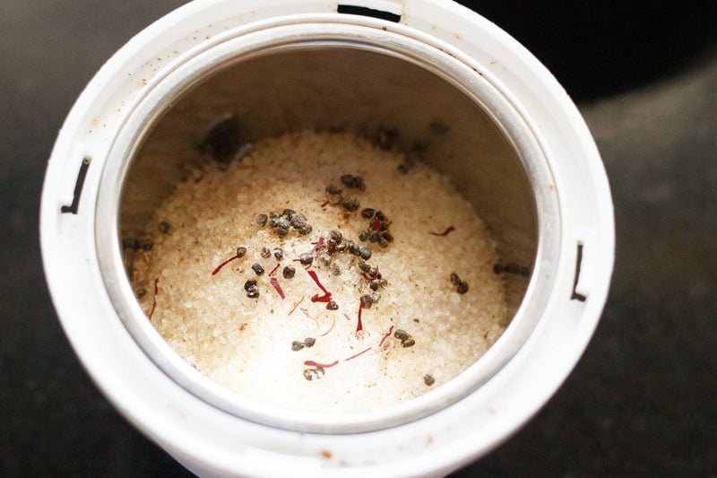 Cardamom seeds, saffron strands and sugar in a grinder.