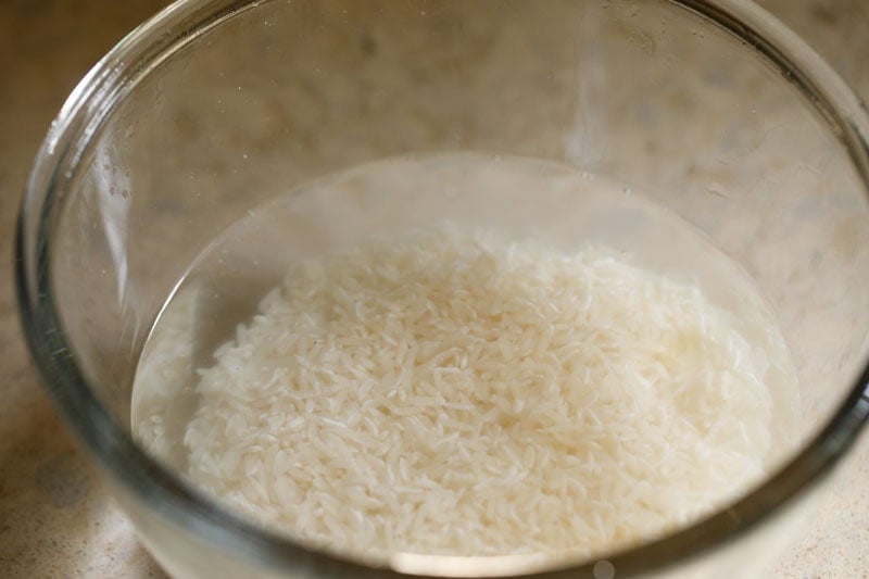Clear water above jasmine rice in glass bowl.