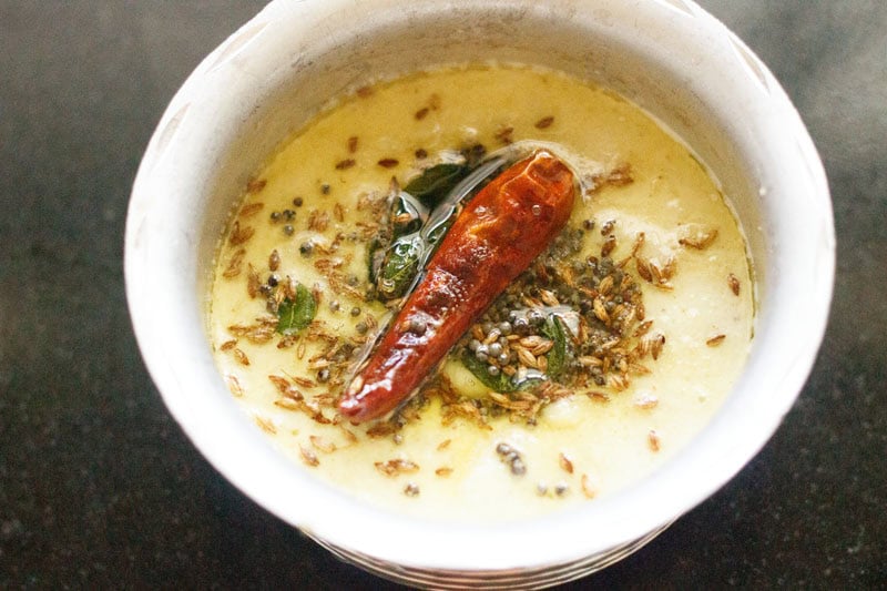 Tempered spices and herbs on idli chutney in a small pan.