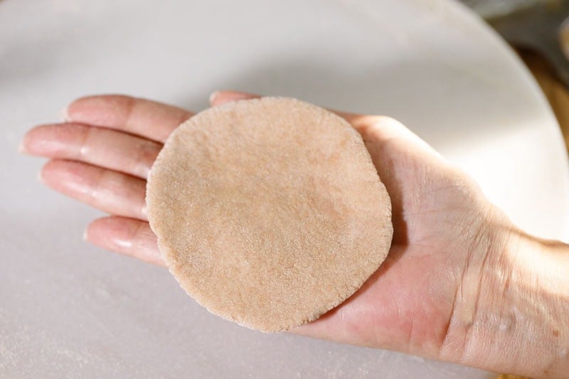 Hand holding round flattened dough piece.