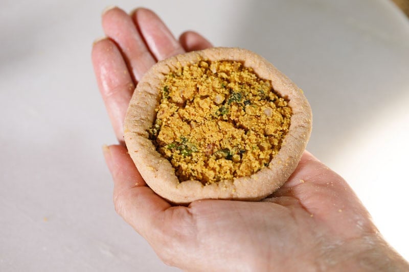 Hand holding filled dough for paratha.