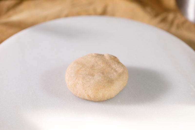 Raw, flattened and stuffed dough ball on a plate.