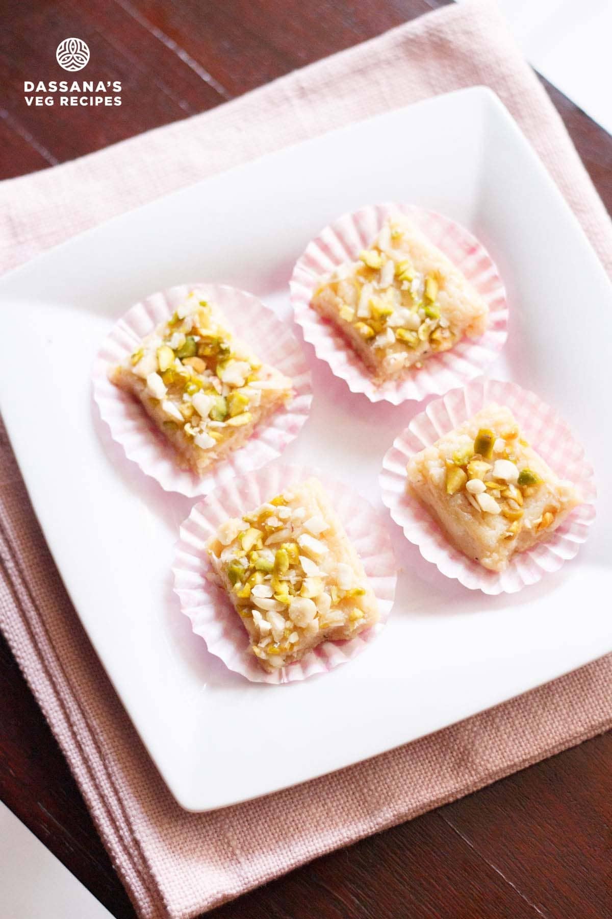 Malai Barfi pieces in pink paper cups on a white plate.