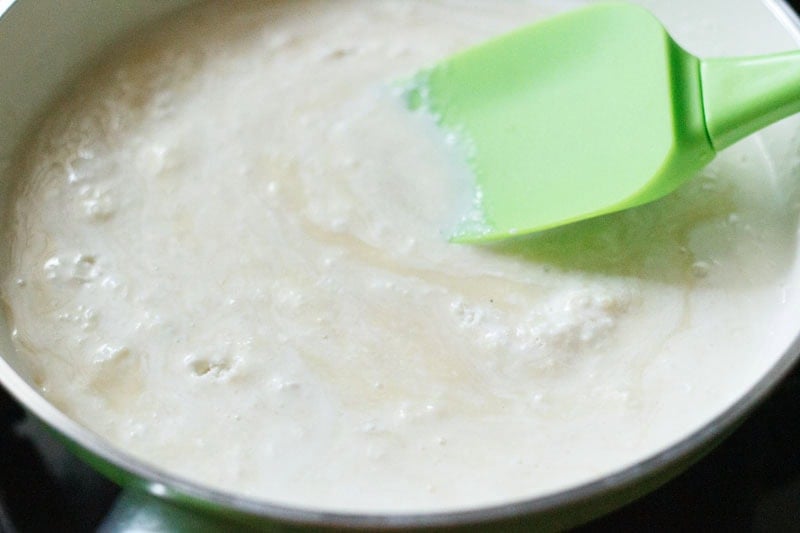 Mixing malai barfi ingredients in pan with green spatula.