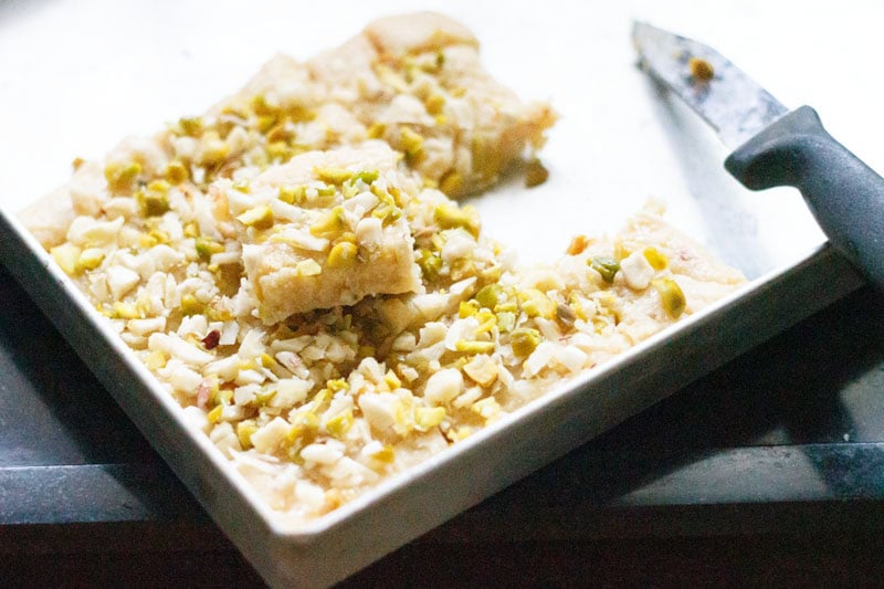 A sliced malai barfi square on tray with a small knife by the side.