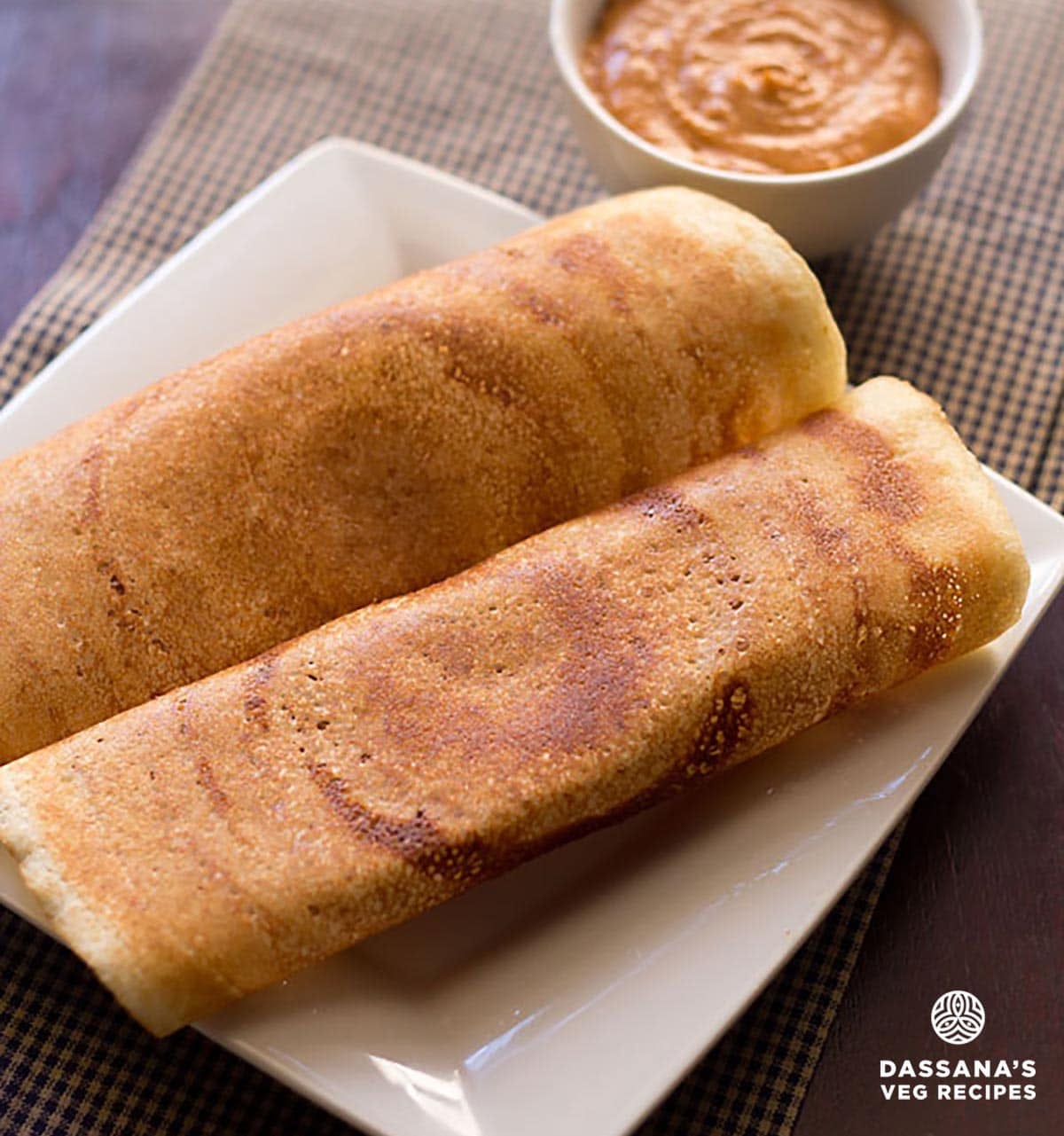 Crispy golden rice dosa on a squared white plate with onion tomato chutney.