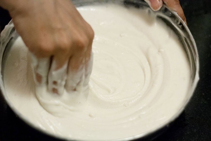 Rice dosa batter being mixed with hands.