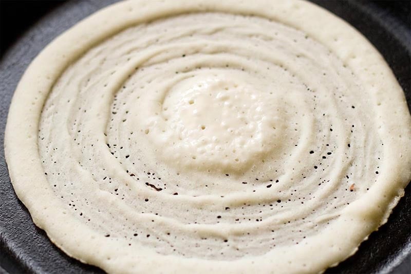 Rice dosa cooking on tawa.