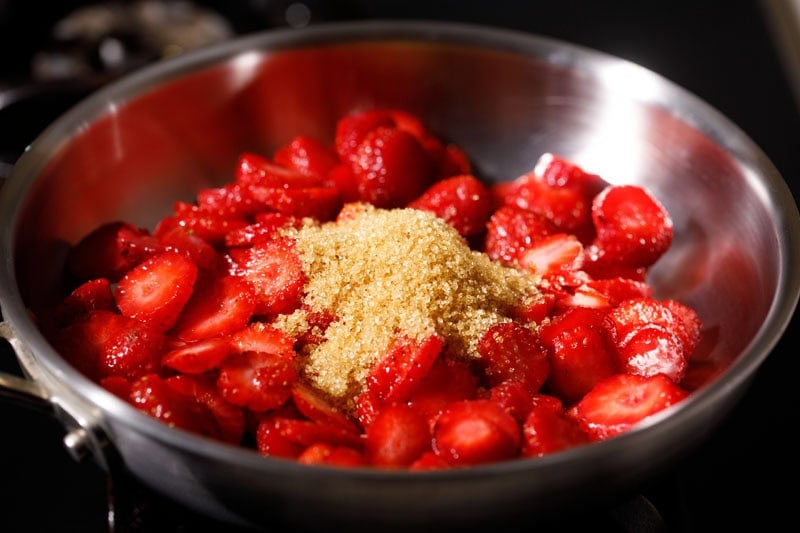 Chopped strawberries with cane sugar on top in a pan.
