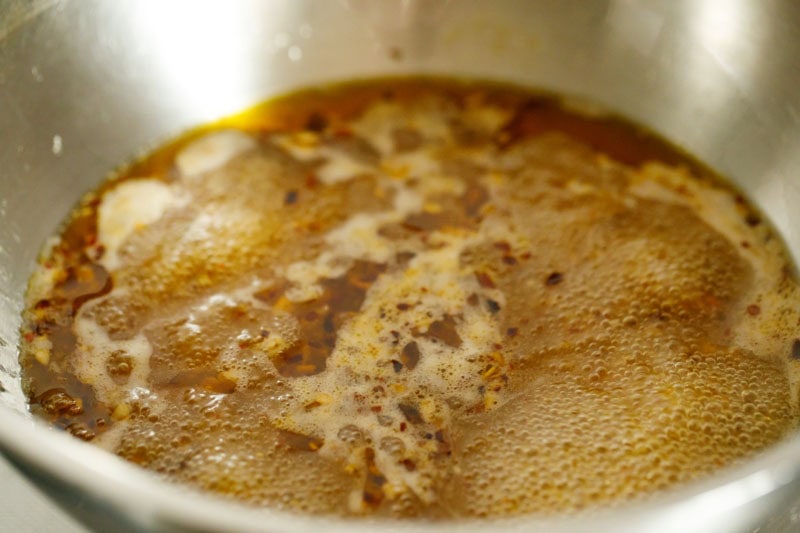 Pasta water added to bubbling olive oil mixture in pan.